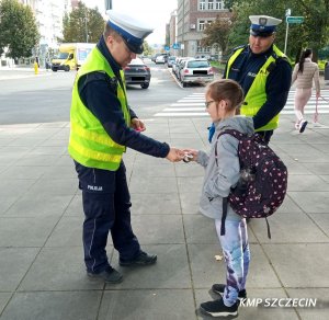 umundurowani policjanci w białych czapkach dają odblask chłopcu