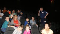 Policjant prowadzi pogadankę z dziećmi na temat bezpieczeństwa w kinie Helios w Szczecinie
